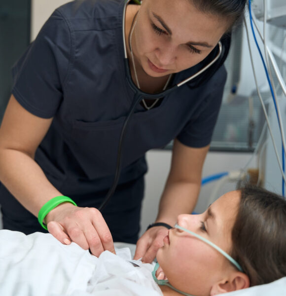 Female doctor standing in ward near young girl and listening with stethoscope in the hospital